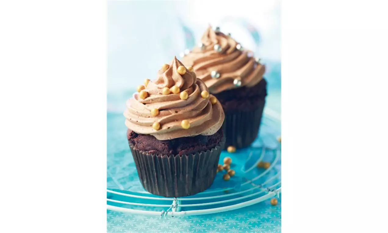 Chokladcupcakes i mörka formar toppade med krämig chokladfrosting och dekorationer av guld- och silverpärlor på ett blått fat