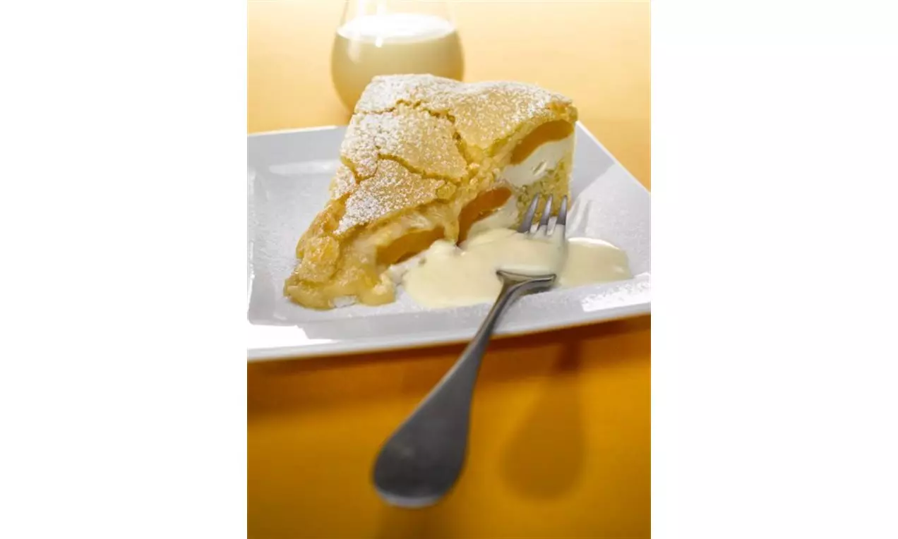 Triangelformad aprikosdessert med gyllene frasig yta pudrad med florsocker, fylld med kräm och serverad med vaniljsås på vit tallrik